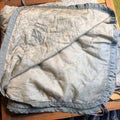 A light beige quilted blanket with a grey ruffled border,