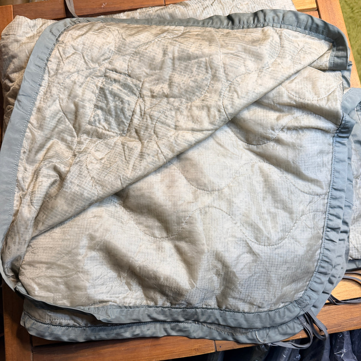 A light beige quilted blanket with a grey ruffled border,