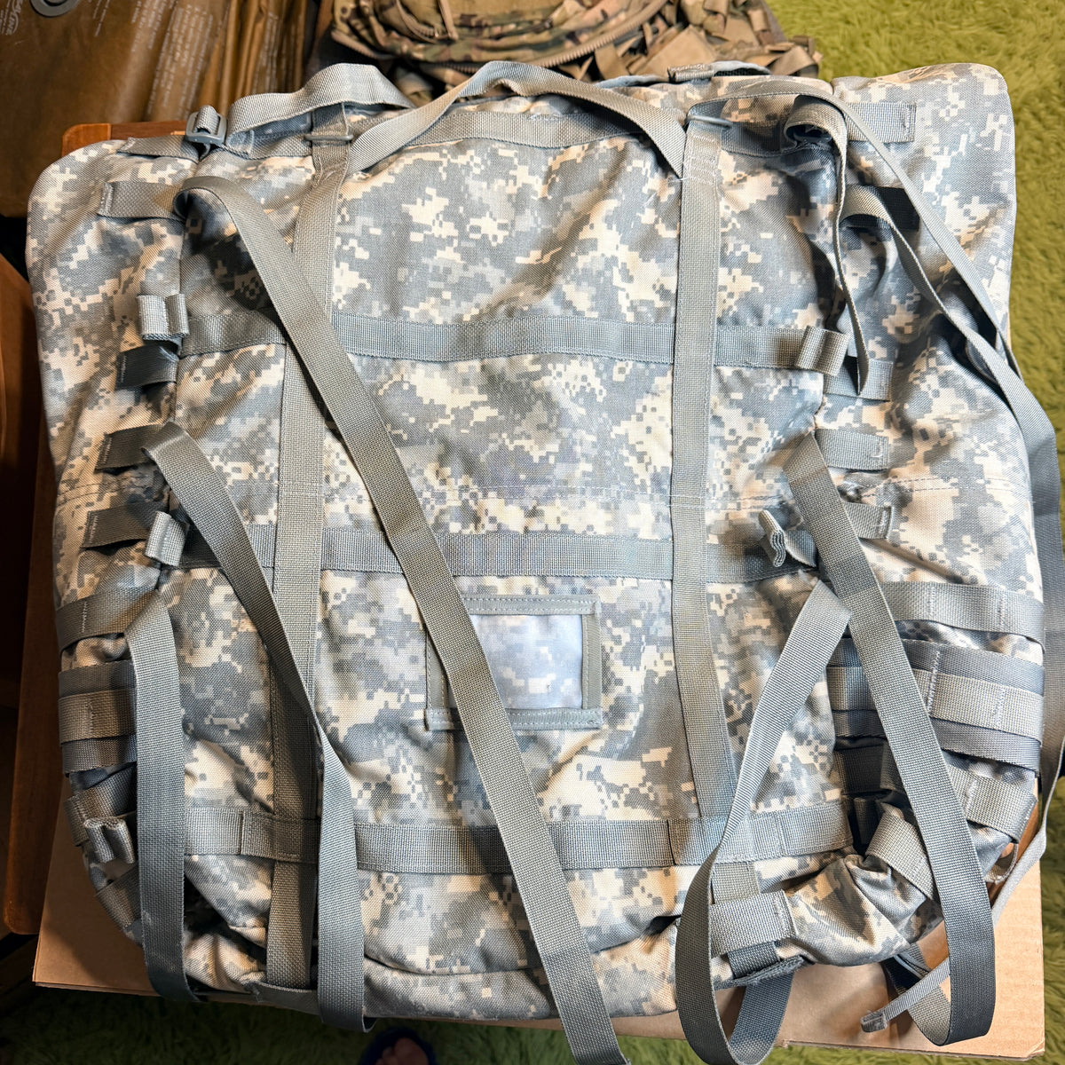 A large military-style gear bag in digital camouflage pattern with multiple gray straps and buckles