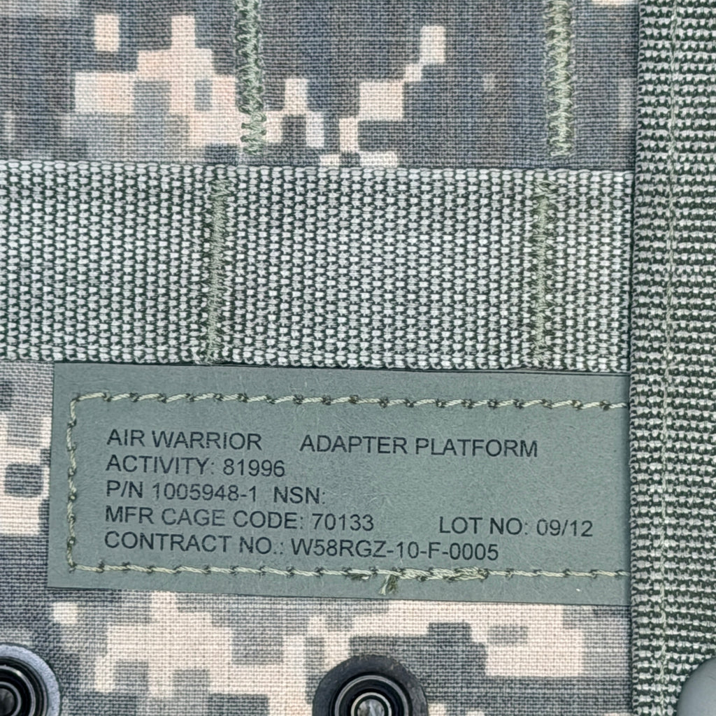 Close-up of a military camouflage fabric with a sewn-in label reading 'AIR WARRIOR ADAPTER PLATFORM' and military-style alphanumeric details.