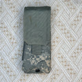 A tactical utility pouch in olive drab and digital camouflage fabric, laid flat on a textured beige and white woven blanket.