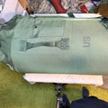 An olive green military-style duffel bag with a top load, a front utility pocket, and a carrying handle.