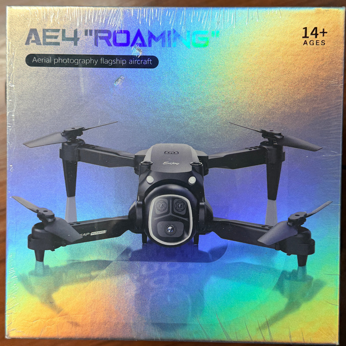 Boxed product for an AE4 'Roaming' aerial photography flagship aircraft, featuring a black quadcopter drone printed on the front over a holographic rainbow gradient background with '14+ AGES' text in the top right.